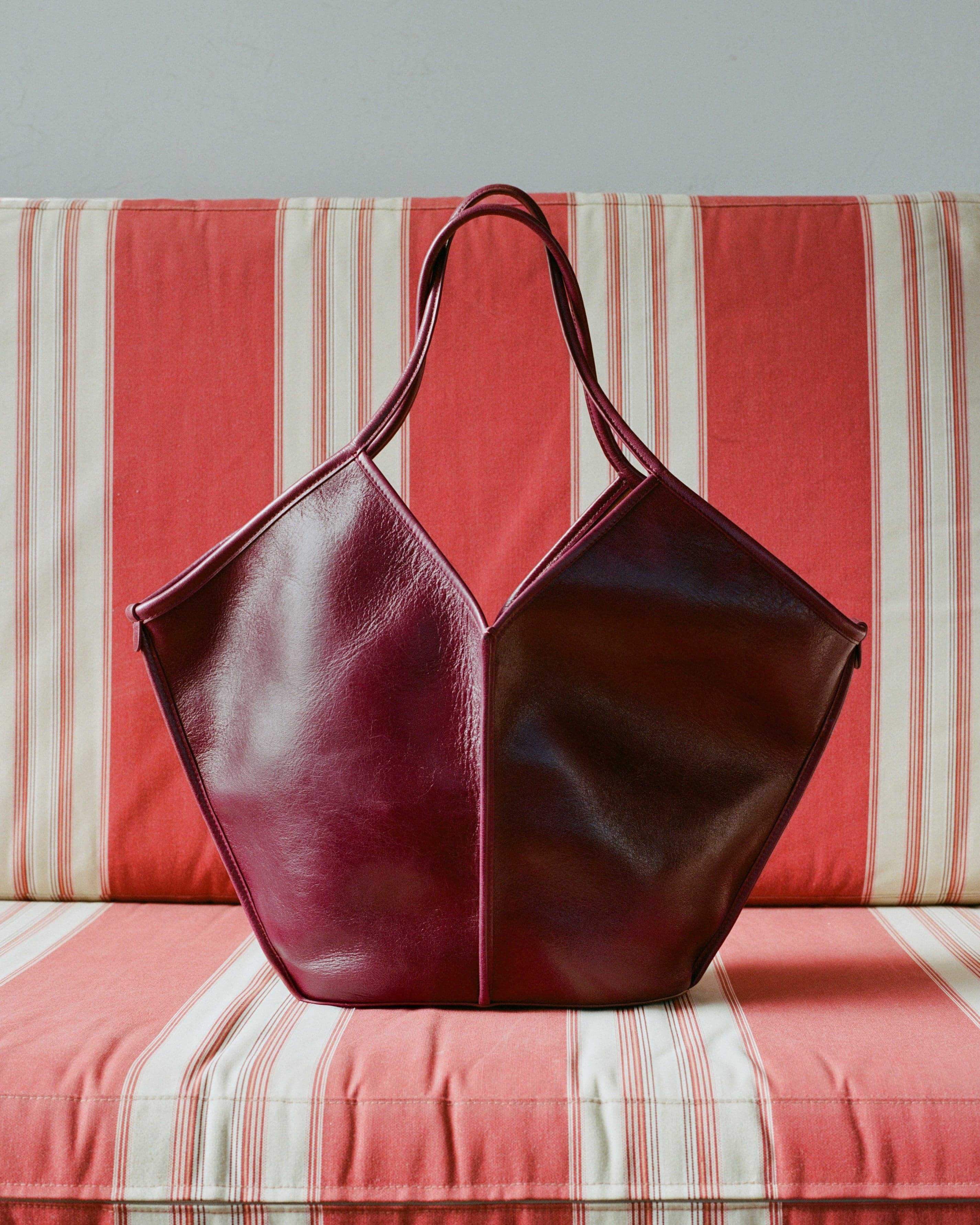 Hereu burgundy leather bag on a red-and-white striped sofa